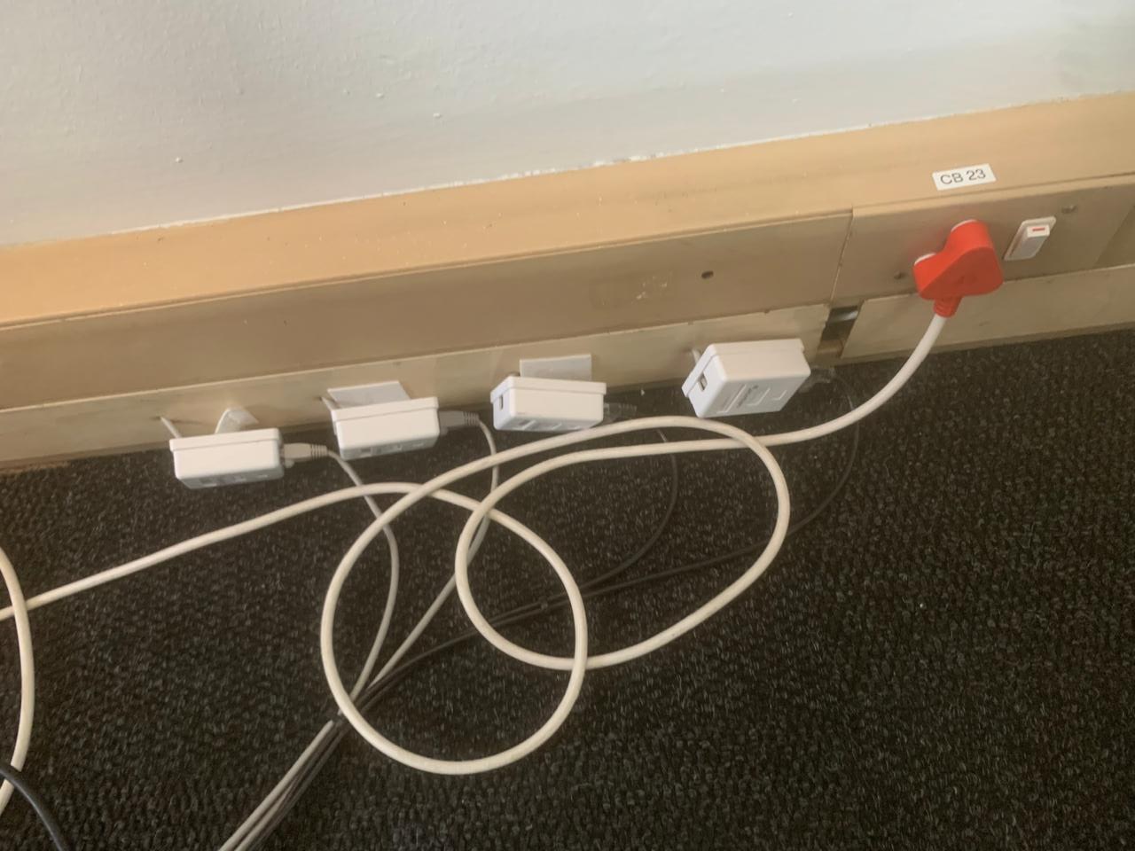 Row of surface-mounted data outlets with loose white cabling running across the carpet
