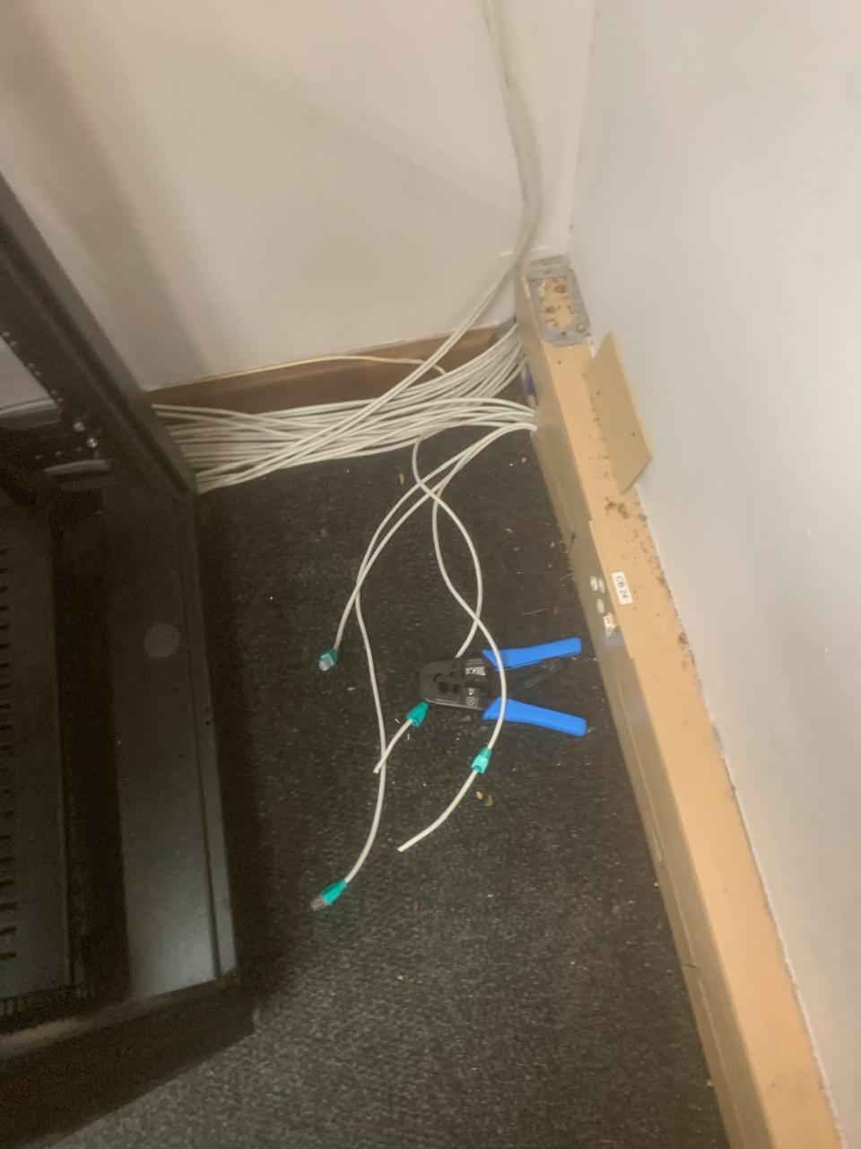 Open network cabinet base with a bundle of unterminated cable and a crimping tool on the floor