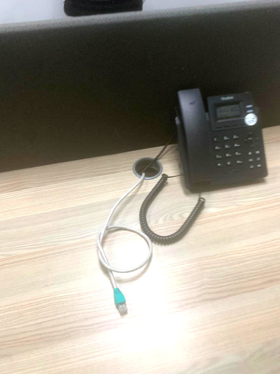 Desk-mounted VoIP handset connected by a patch lead through the desk cable port